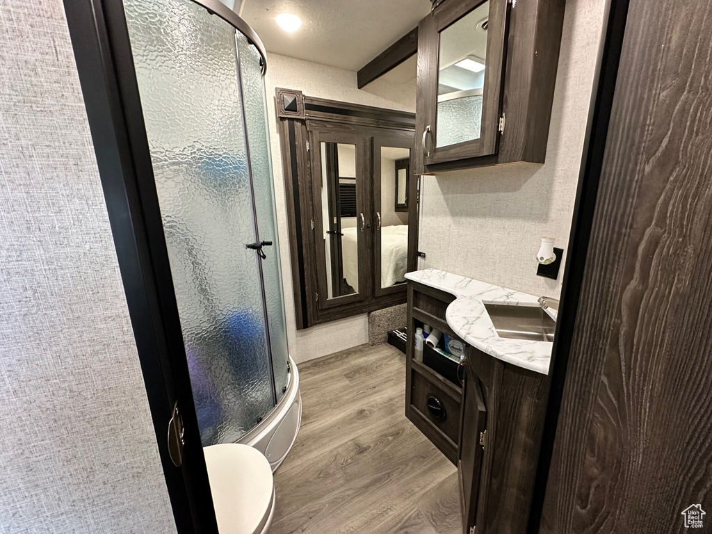 Bathroom featuring a shower with door, vanity, toilet, and hardwood / wood-style flooring