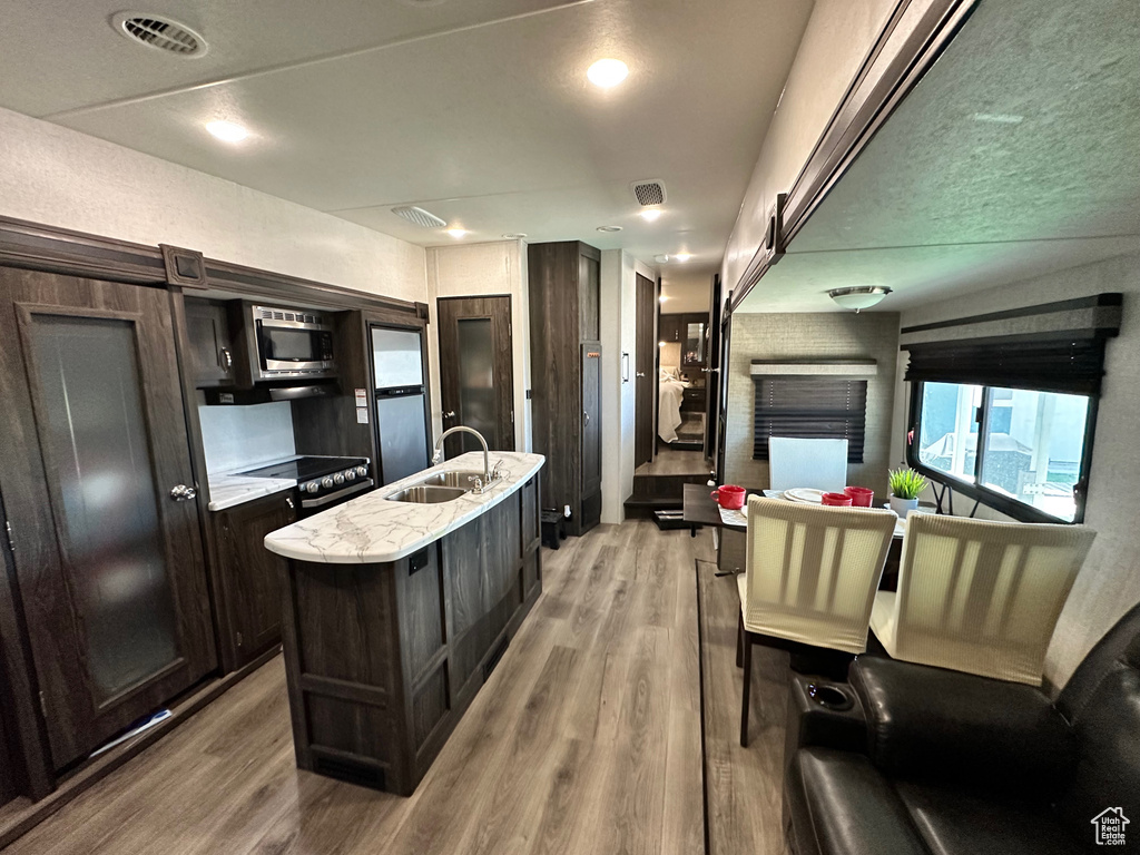 Kitchen with light hardwood / wood-style flooring, a center island with sink, sink, and dark brown cabinetry