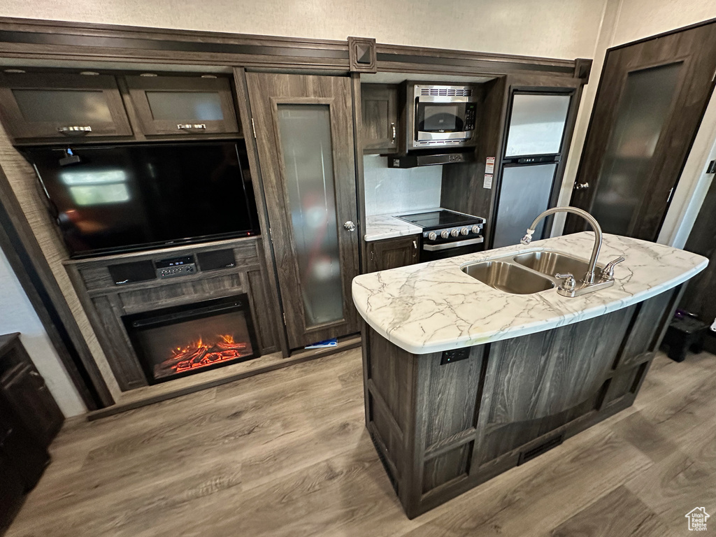 Kitchen featuring dark brown cabinetry, light wood-type flooring, a kitchen island with sink, and sink