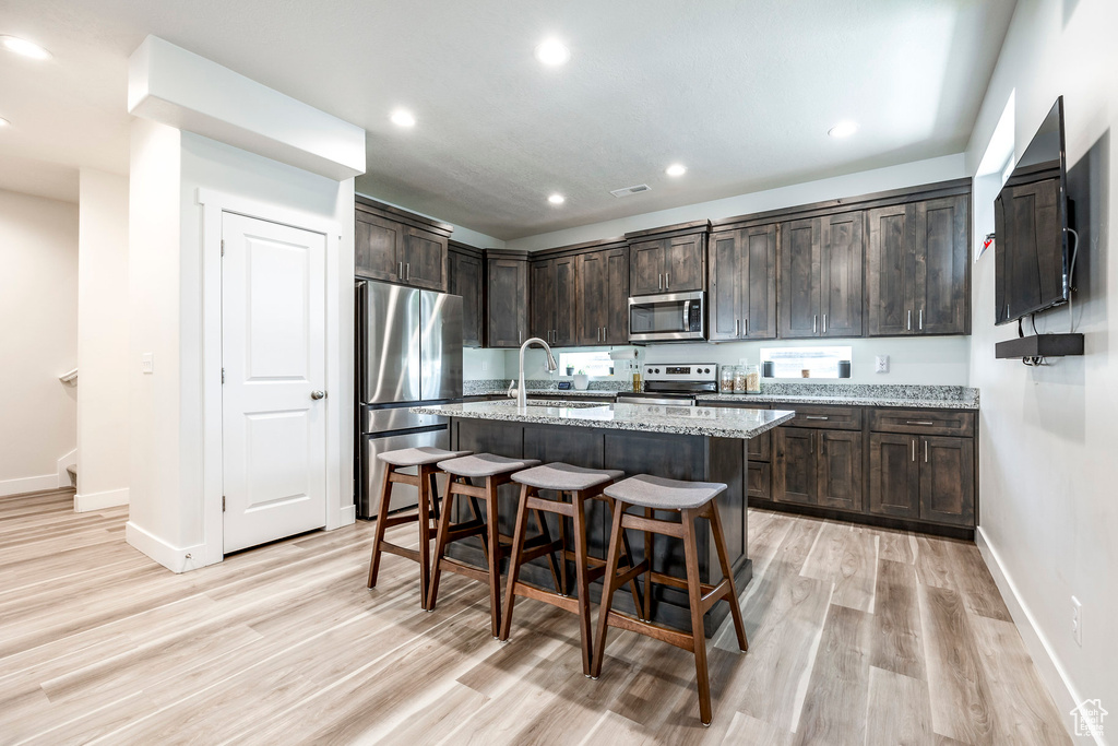 Kitchen featuring light wood-type flooring, sink, dark brown cabinets, stainless steel appliances, and light stone countertops