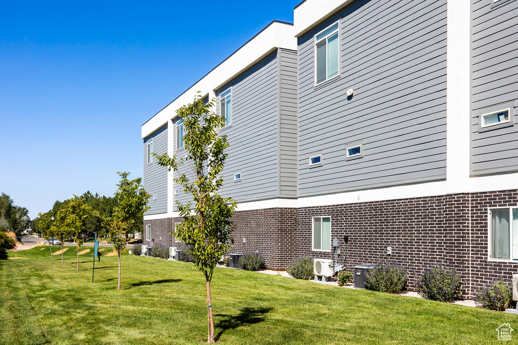 View of side of property with brick siding, a lawn, and cooling unit
