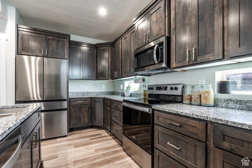 Kitchen with light hardwood / wood-style flooring, stainless steel appliances, light stone counters, and dark brown cabinetry