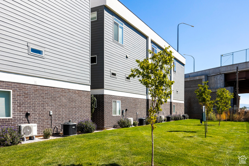 View of home's exterior featuring central air condition unit, brick siding, a cooling unit, and a yard