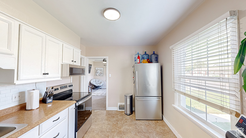 Kitchen featuring backsplash, stainless steel appliances, and white cabinets