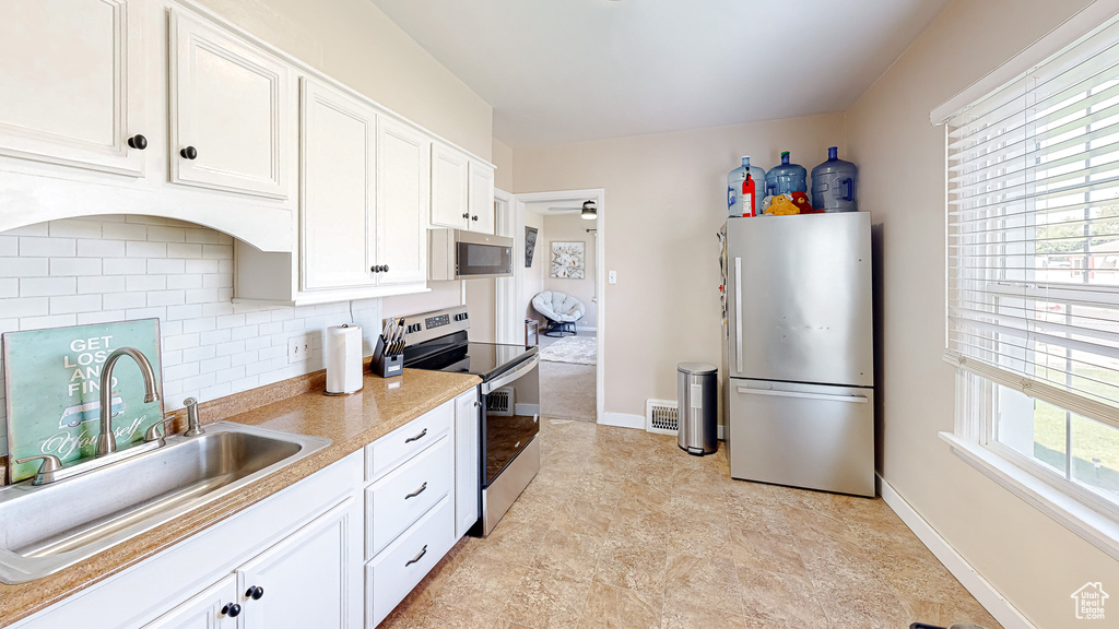 Kitchen featuring a healthy amount of sunlight, stainless steel appliances, white cabinetry, and sink