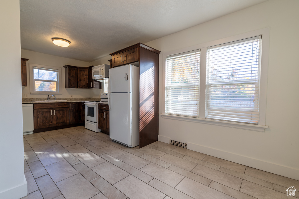 Kitchen featuring white appliances, light tile patterned floors, light stone countertops, dark brown cabinetry, and sink