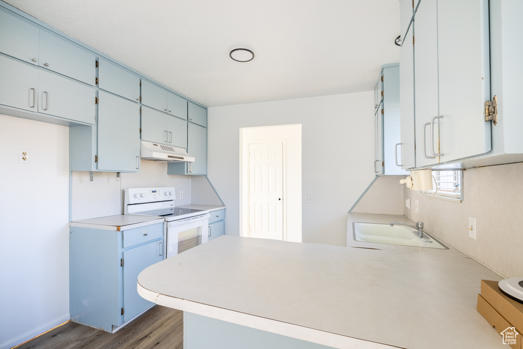 Kitchen featuring dark wood-type flooring, sink, kitchen peninsula, white electric range oven, and blue cabinetry