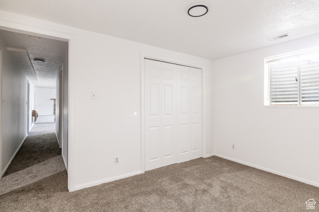 Unfurnished bedroom featuring a textured ceiling, carpet flooring, and a closet