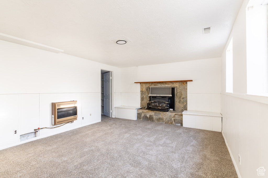 Unfurnished living room featuring a stone fireplace, heating unit, and carpet