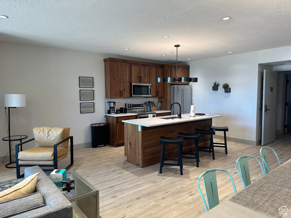 Kitchen featuring sink, decorative light fixtures, a center island with sink, appliances with stainless steel finishes, and light wood-type flooring