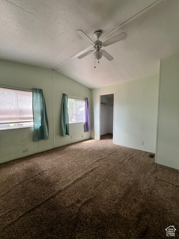 Empty room featuring lofted ceiling, ceiling fan, carpet floors, and a textured ceiling
