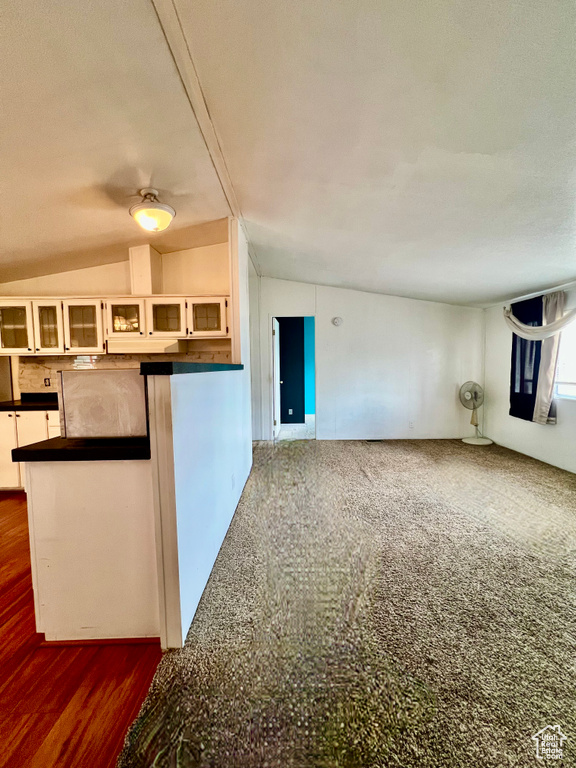 Kitchen featuring vaulted ceiling, white cabinetry, dark carpet, and kitchen peninsula