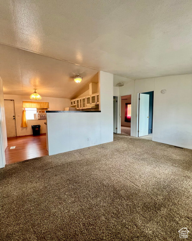 Unfurnished living room featuring lofted ceiling, a textured ceiling, and carpet floors