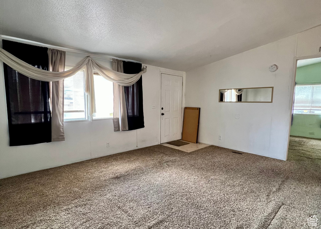 Interior space featuring a textured ceiling, vaulted ceiling, and carpet floors