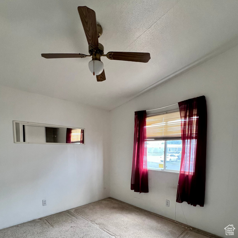 Unfurnished room featuring lofted ceiling, ceiling fan, carpet, and a textured ceiling