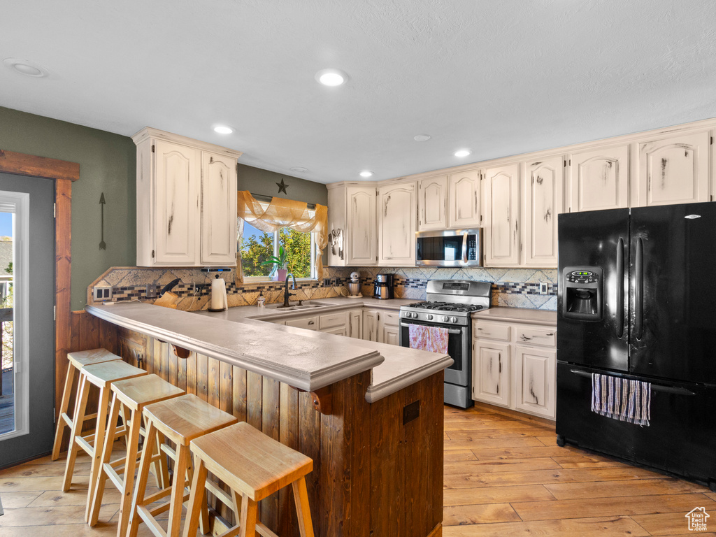 Kitchen with a breakfast bar area, kitchen peninsula, sink, light wood-type flooring, and appliances with stainless steel finishes