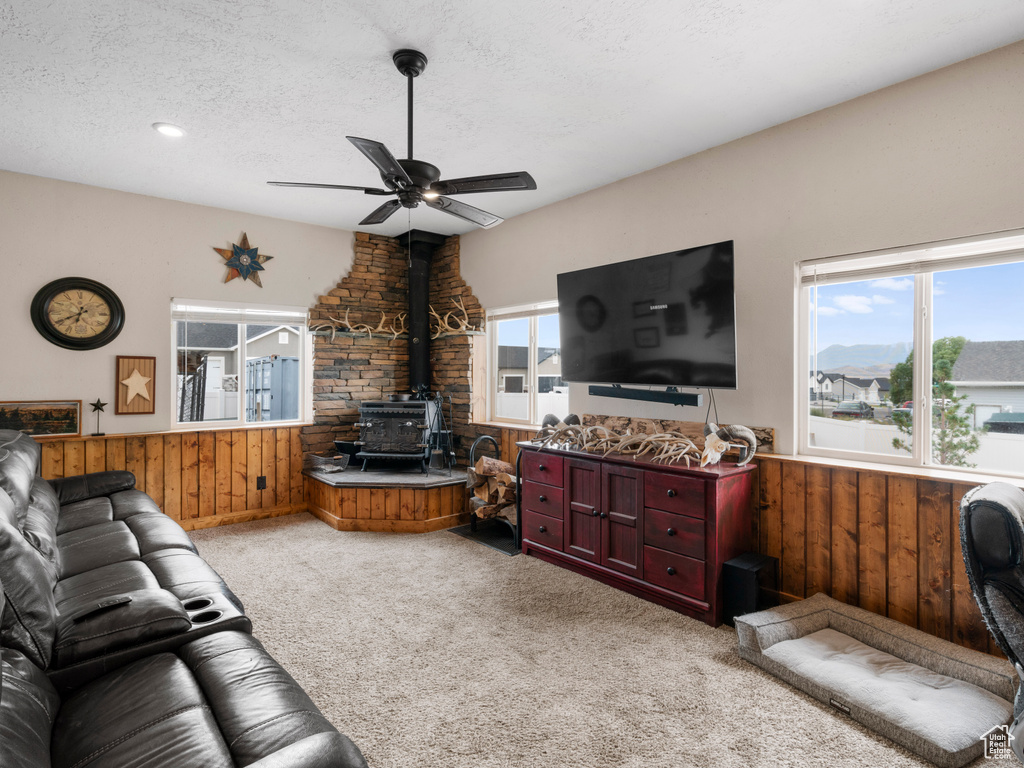 Living room with wood walls, a wood stove, a textured ceiling, ceiling fan, and light colored carpet