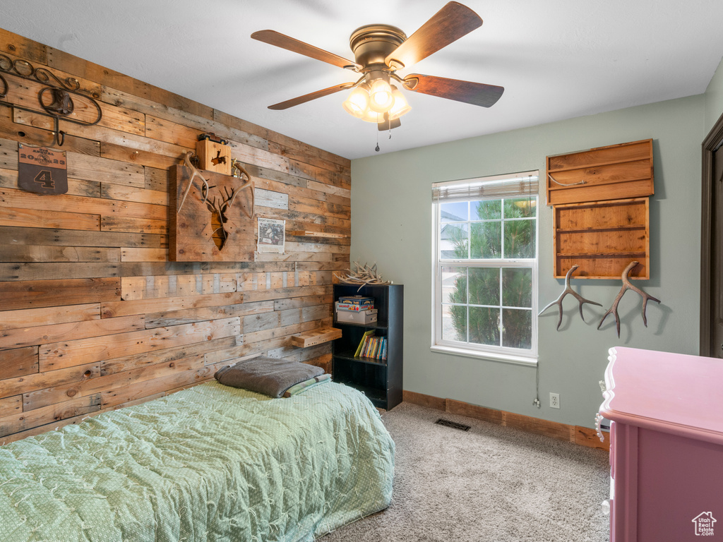 Carpeted bedroom featuring wooden walls and ceiling fan