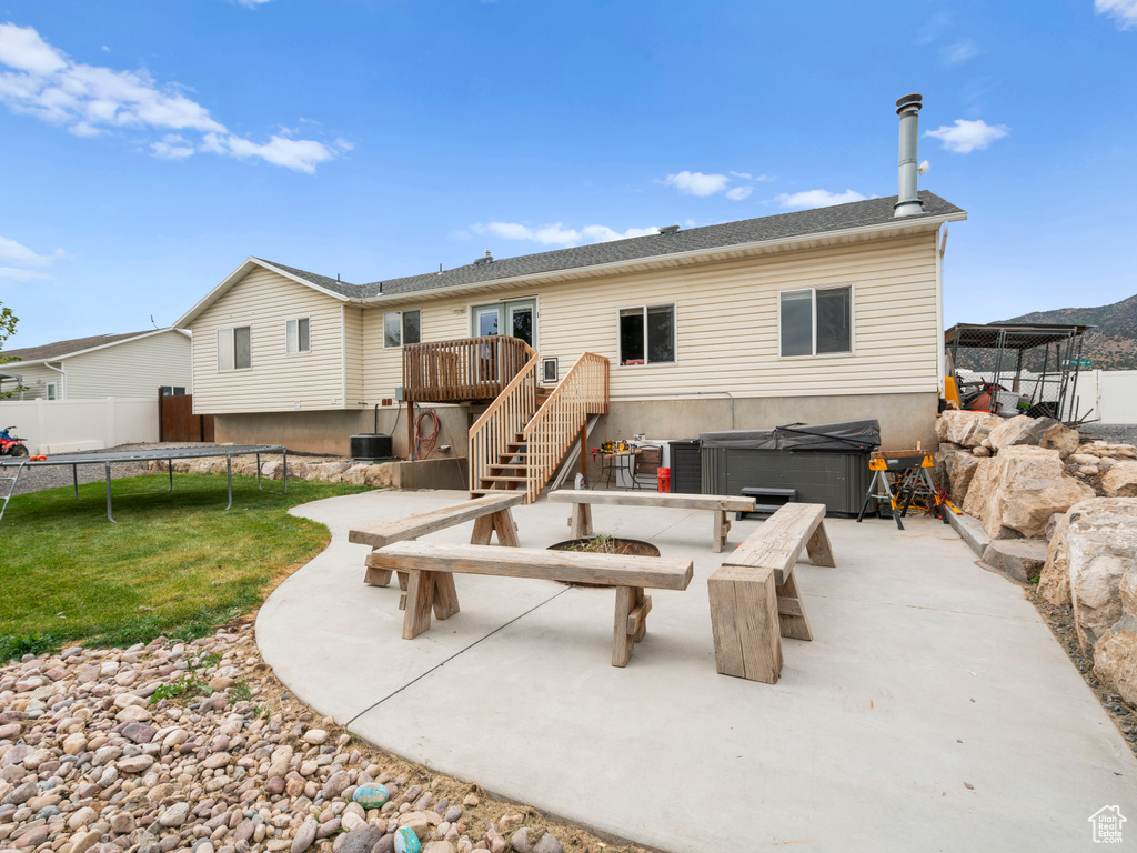 Back of property featuring cooling unit, a patio, a deck, a yard, and a hot tub