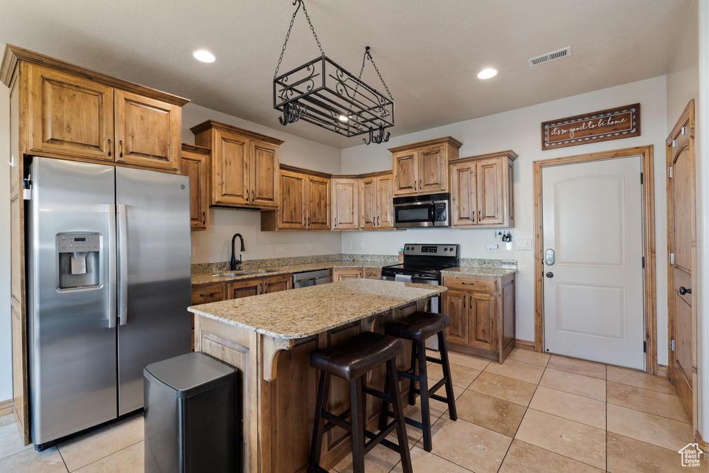 Kitchen with appliances with stainless steel finishes, light stone countertops, sink, a kitchen breakfast bar, and a kitchen island