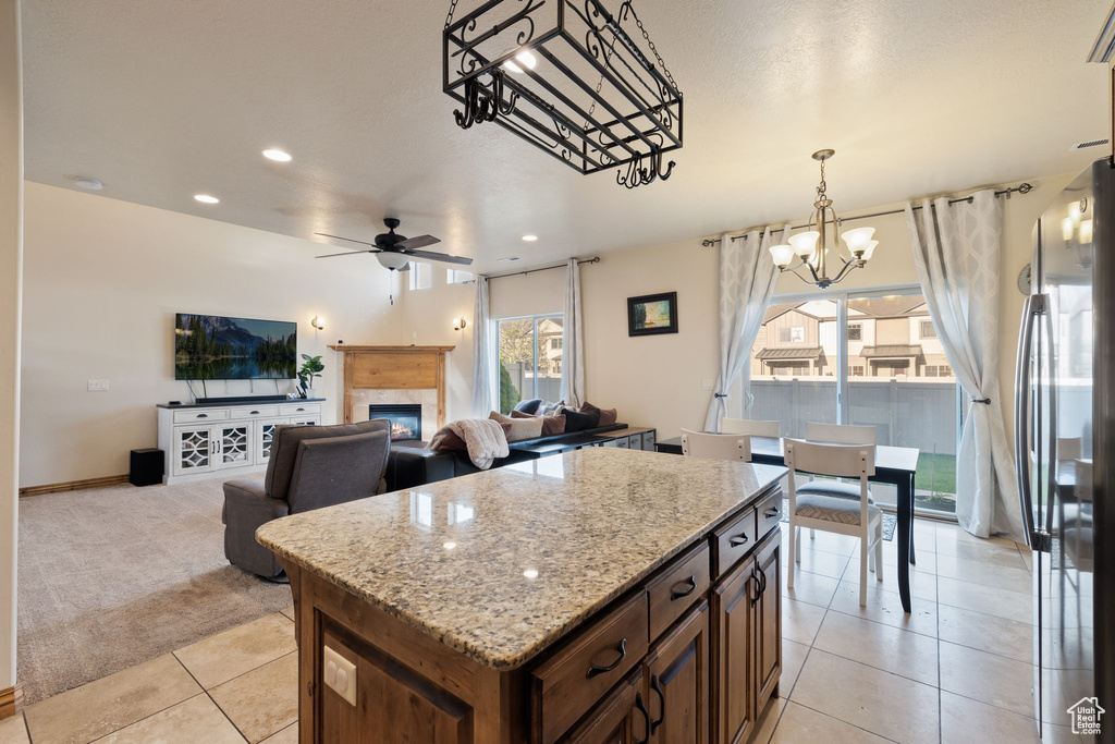 Kitchen featuring ceiling fan with notable chandelier, stainless steel fridge, light stone counters, a center island, and light colored carpet