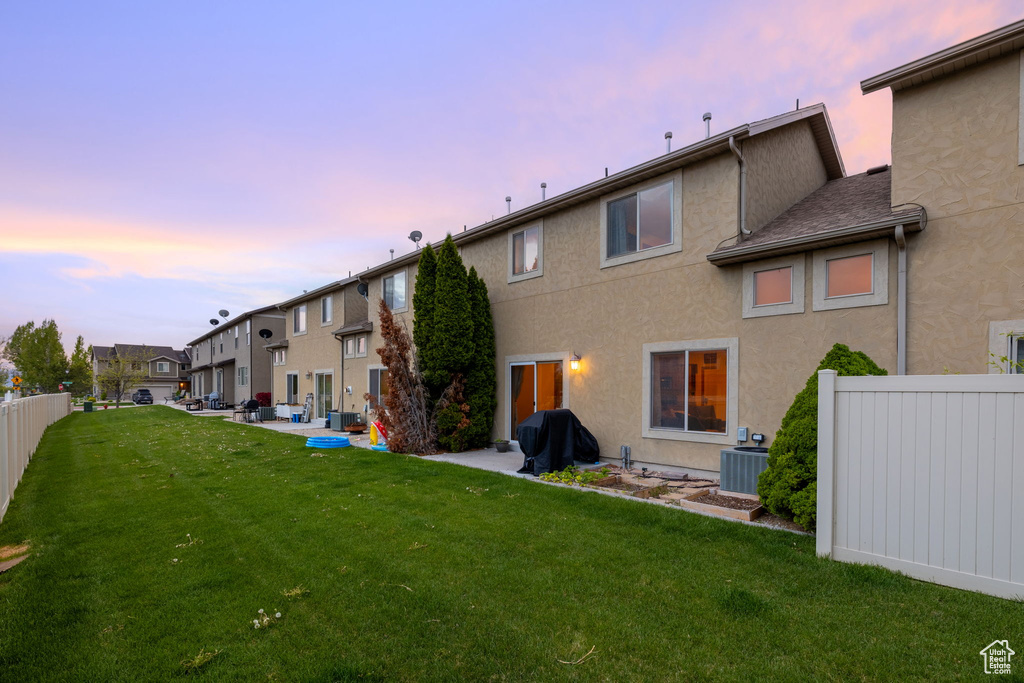 Back house at dusk featuring a yard, cooling unit, and a patio area