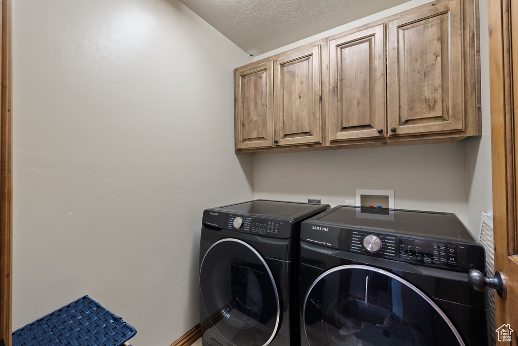 Laundry area featuring washing machine and clothes dryer, cabinets, and a textured ceiling