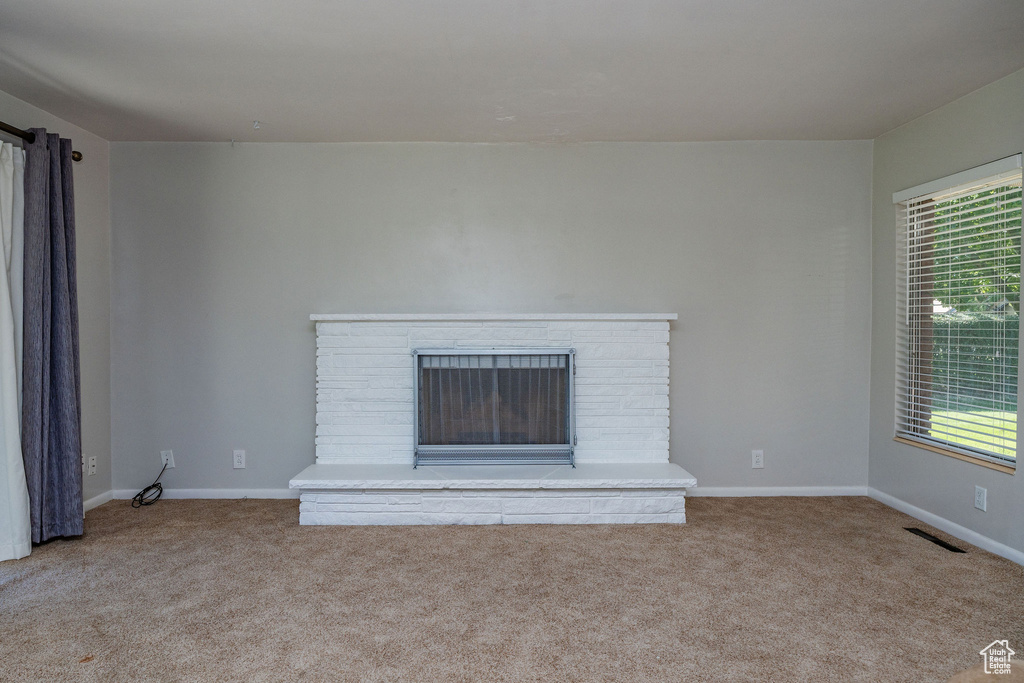 Unfurnished living room with light colored carpet and a brick fireplace