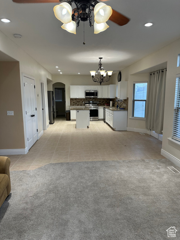 Kitchen with ceiling fan with notable chandelier, pendant lighting, light carpet, stainless steel appliances, and white cabinetry