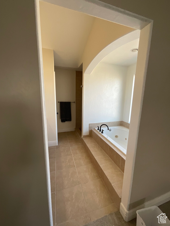 Bathroom featuring tile patterned flooring, a relaxing tiled tub, and vaulted ceiling