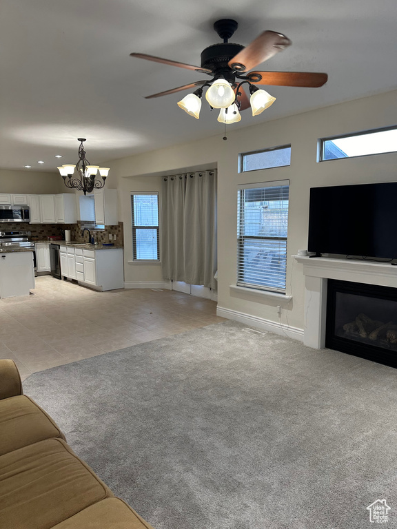 Unfurnished living room with ceiling fan with notable chandelier and a wealth of natural light