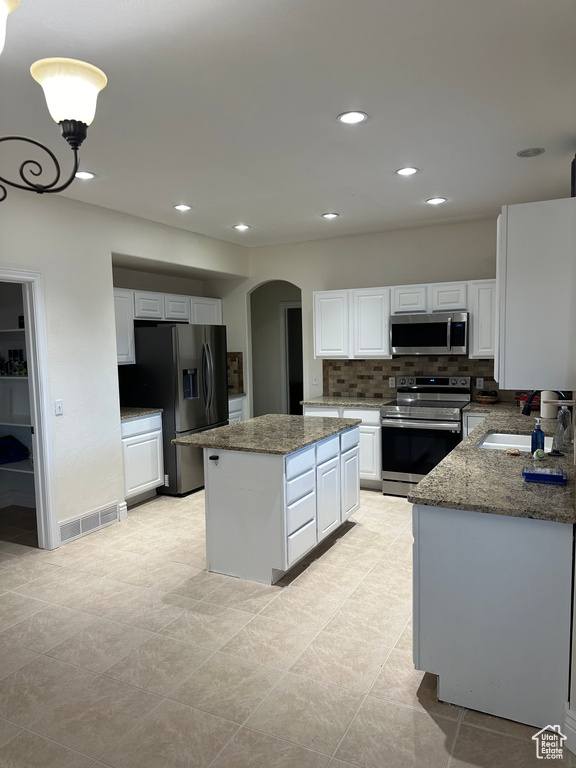 Kitchen with white cabinets, a center island, stainless steel appliances, stone countertops, and sink