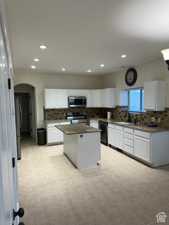 Kitchen with a kitchen island, light stone counters, appliances with stainless steel finishes, and white cabinetry