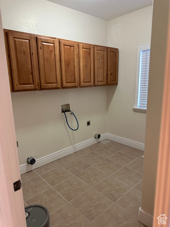 Clothes washing area with hookup for a washing machine, light tile patterned floors, hookup for an electric dryer, and cabinets