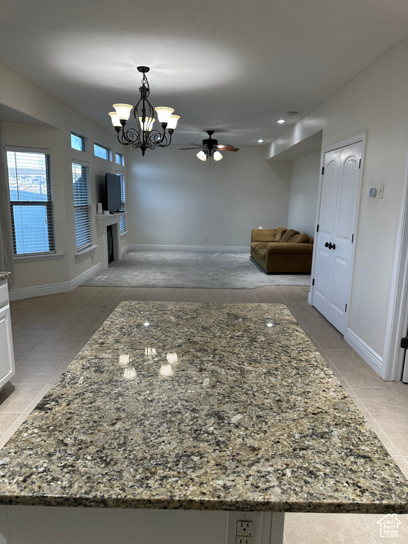 Interior space featuring pendant lighting, dark stone counters, ceiling fan with notable chandelier, and white cabinets