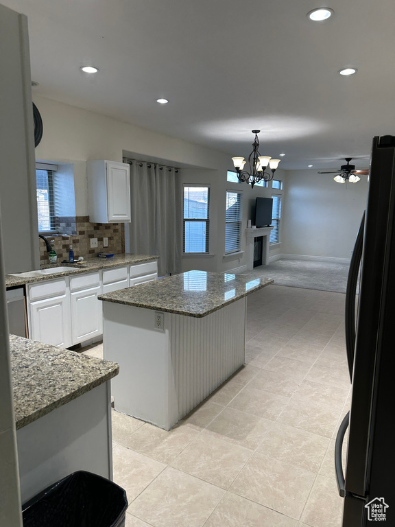 Kitchen with pendant lighting, stainless steel refrigerator, ceiling fan with notable chandelier, a center island, and white cabinets