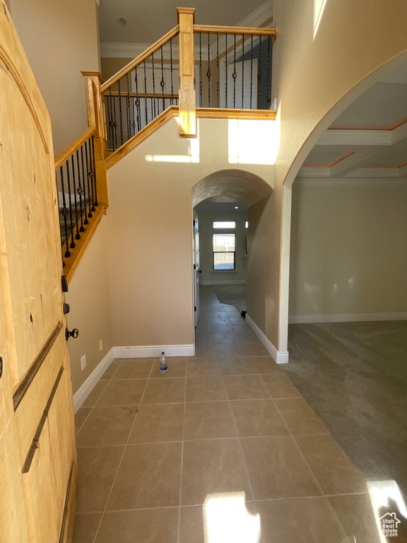 Entrance foyer with a high ceiling, coffered ceiling, tile patterned floors, and ornamental molding