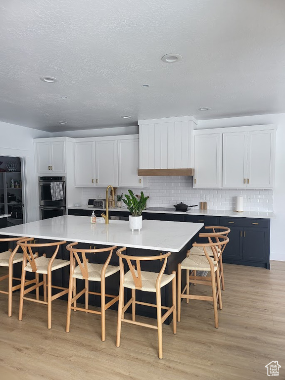 Kitchen with white cabinets, a kitchen breakfast bar, stainless steel double oven, and light hardwood / wood-style flooring