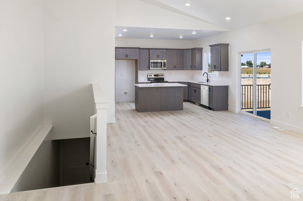 Kitchen with a center island, sink, vaulted ceiling, light hardwood / wood-style flooring, and stainless steel appliances