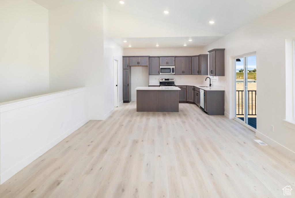 Kitchen featuring lofted ceiling, sink, stainless steel appliances, a center island, and light wood-type flooring