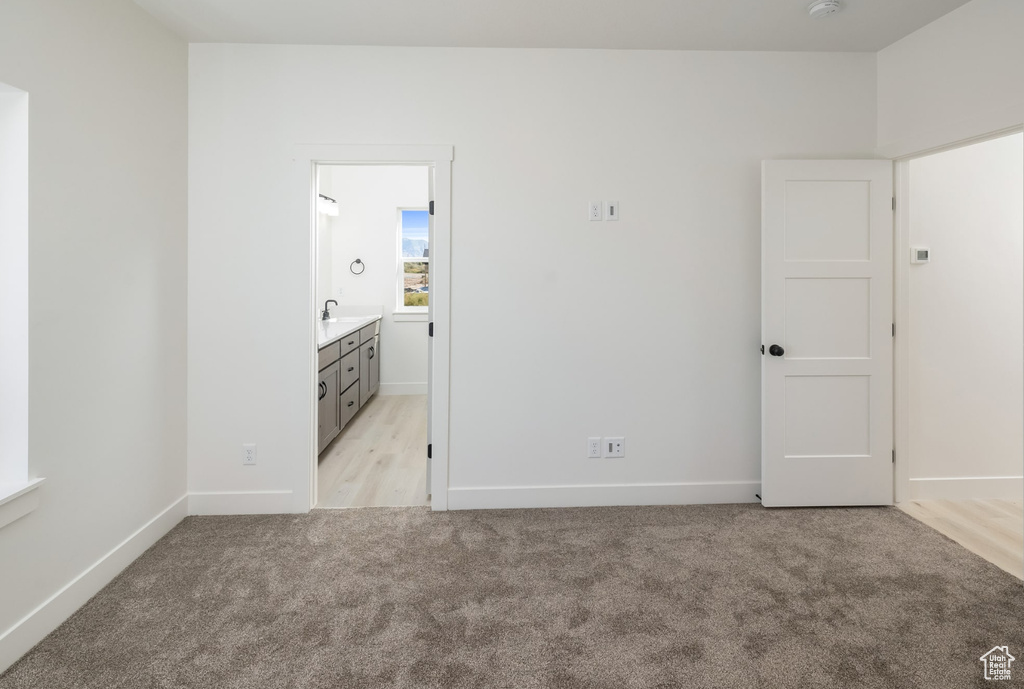 Unfurnished bedroom featuring connected bathroom, light colored carpet, and sink