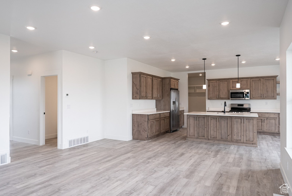 Kitchen featuring light hardwood / wood-style floors, an island with sink, stainless steel appliances, decorative light fixtures, and sink