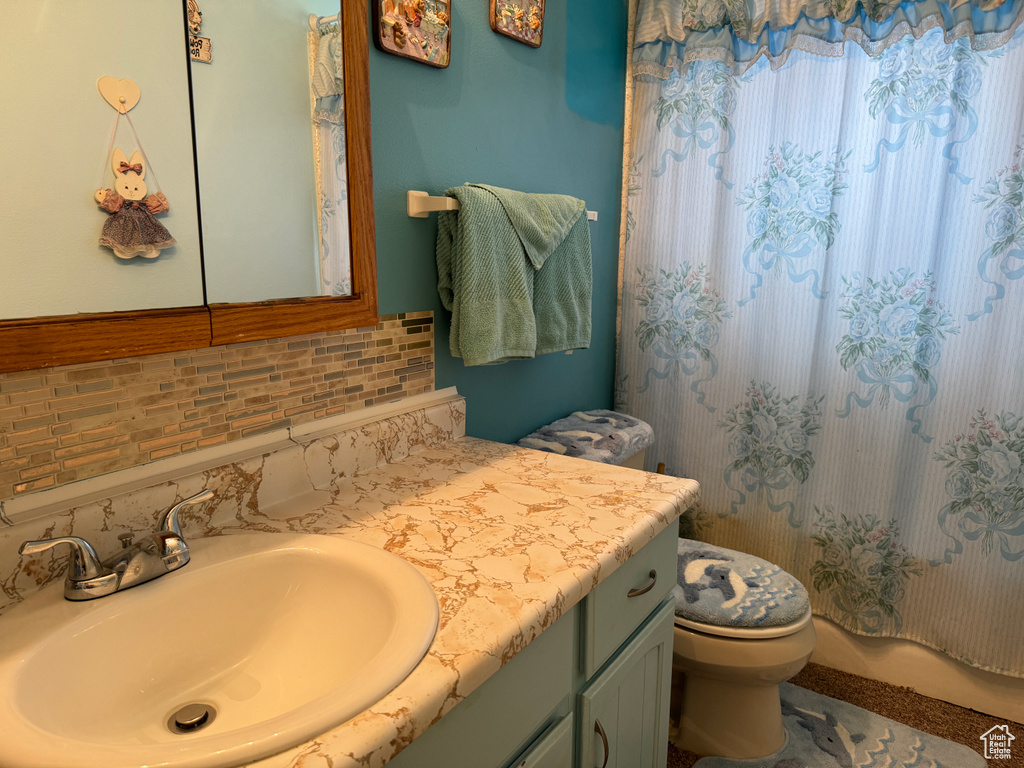 Bathroom featuring a shower with shower curtain, toilet, decorative backsplash, and vanity