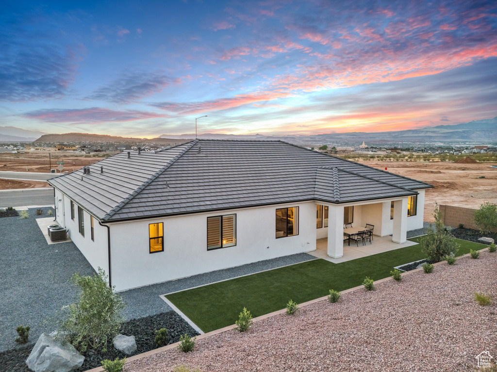 Back house at dusk featuring a mountain view, a lawn, a patio area, and central AC