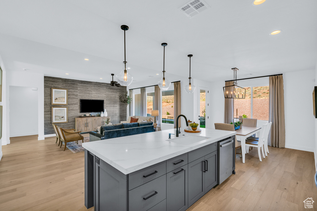 Kitchen featuring light stone counters, sink, an island with sink, hanging light fixtures, and light hardwood / wood-style flooring