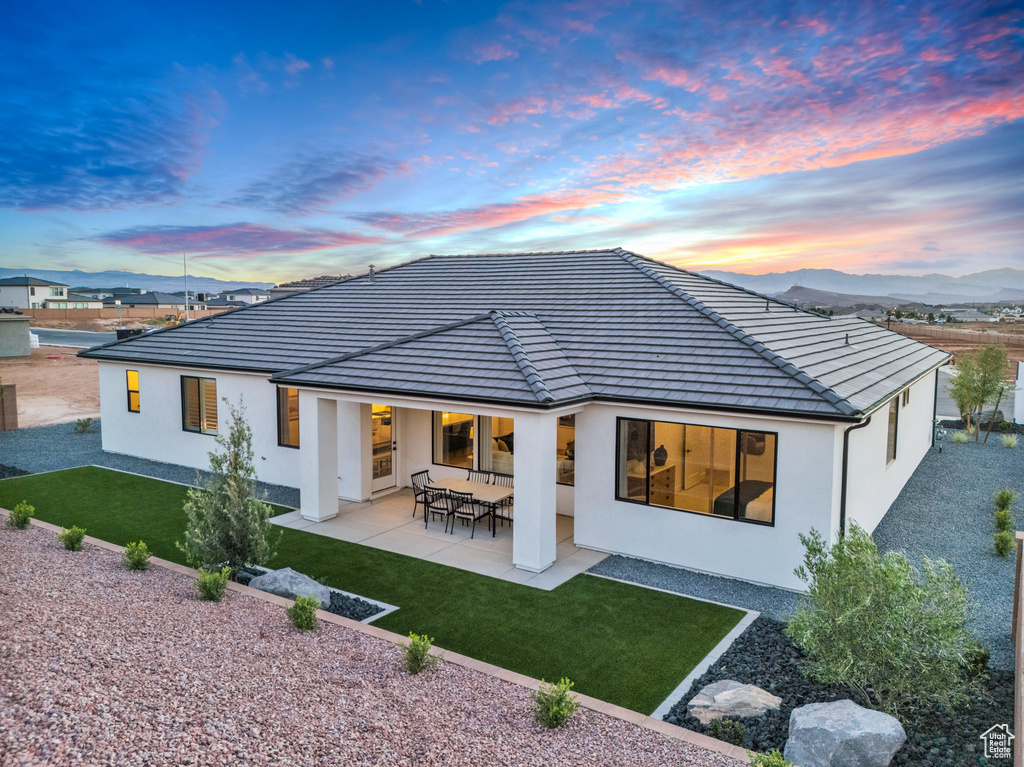 Back house at dusk featuring a lawn, a patio, and a mountain view