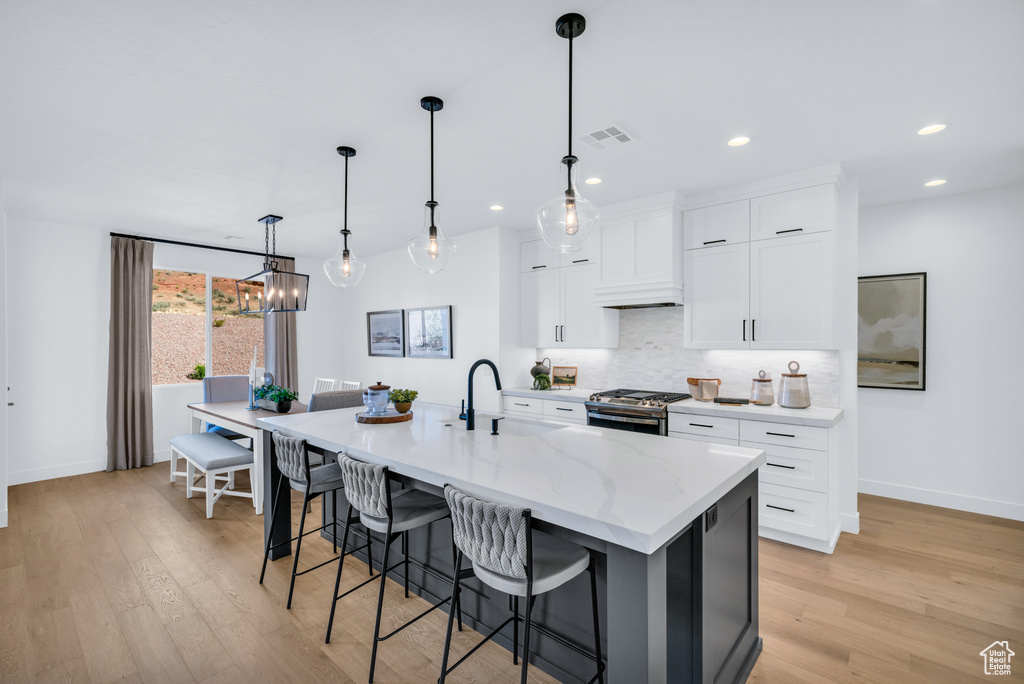 Kitchen featuring light hardwood / wood-style floors, an island with sink, white cabinets, gas range, and decorative light fixtures