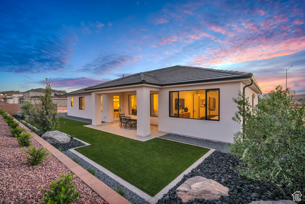 Back house at dusk with a yard and a patio area