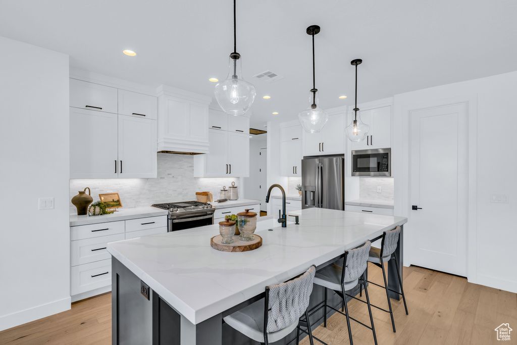 Kitchen featuring light hardwood / wood-style flooring, white cabinetry, appliances with stainless steel finishes, and a kitchen island with sink