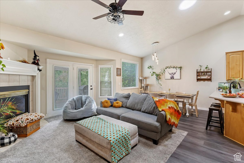 Living room with lofted ceiling, a tiled fireplace, ceiling fan, and dark hardwood / wood-style flooring